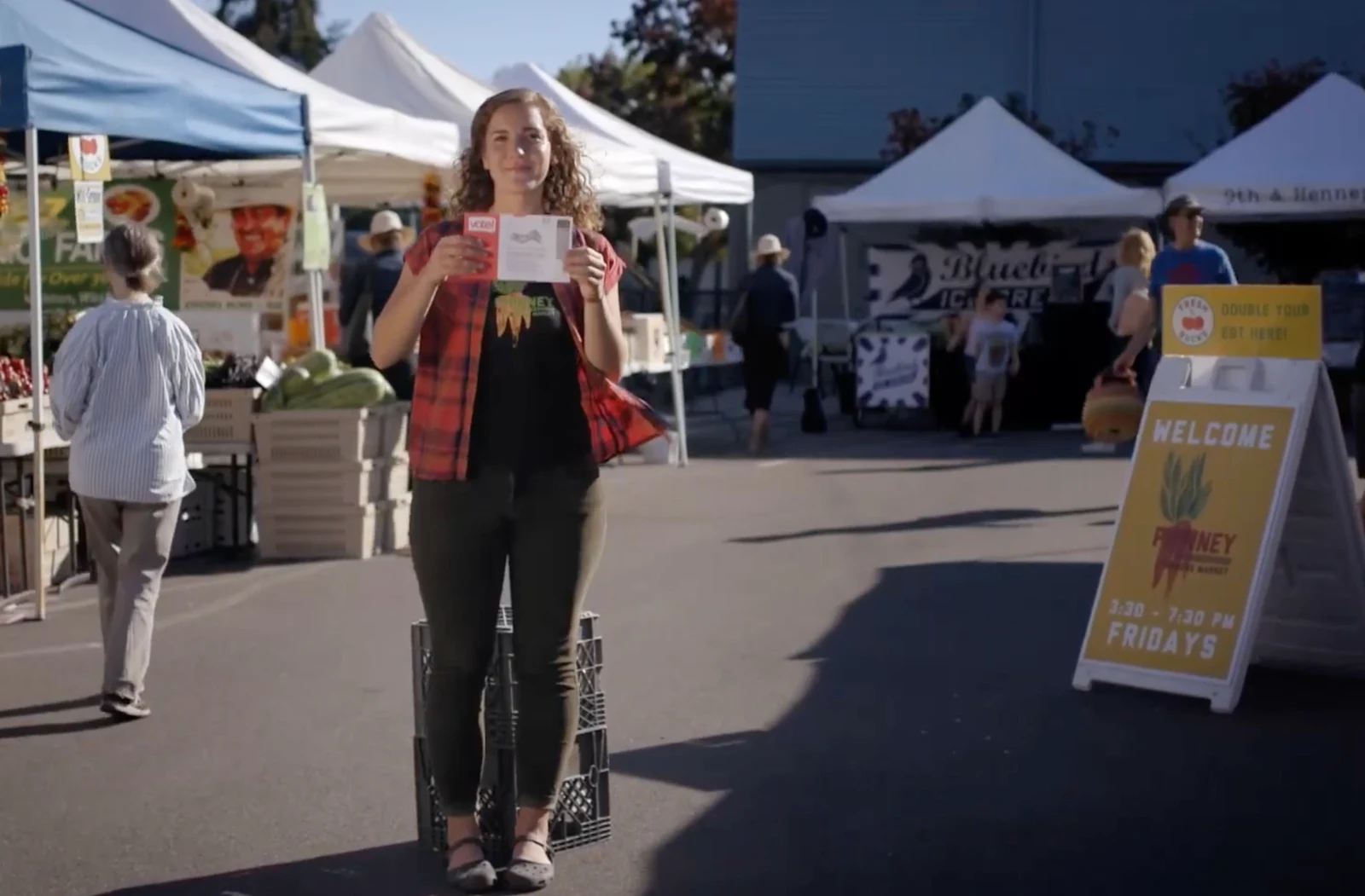 A participant holding voting materials at an outdoor farmers market in the King County Elections campaign