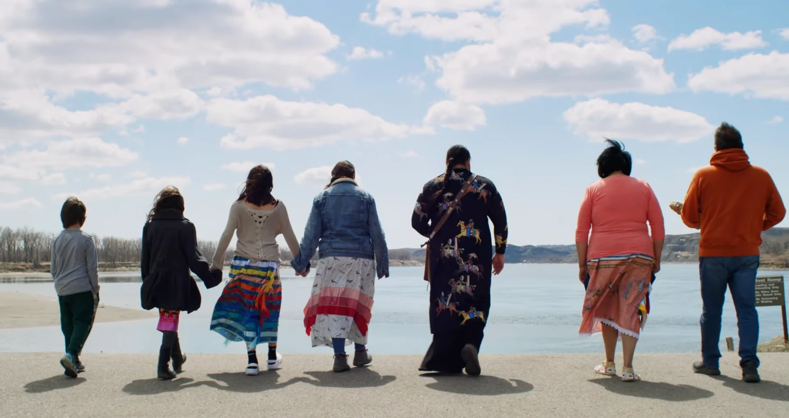 Seven people walking toward a river beneath a blue sky in Tahnaanooku’